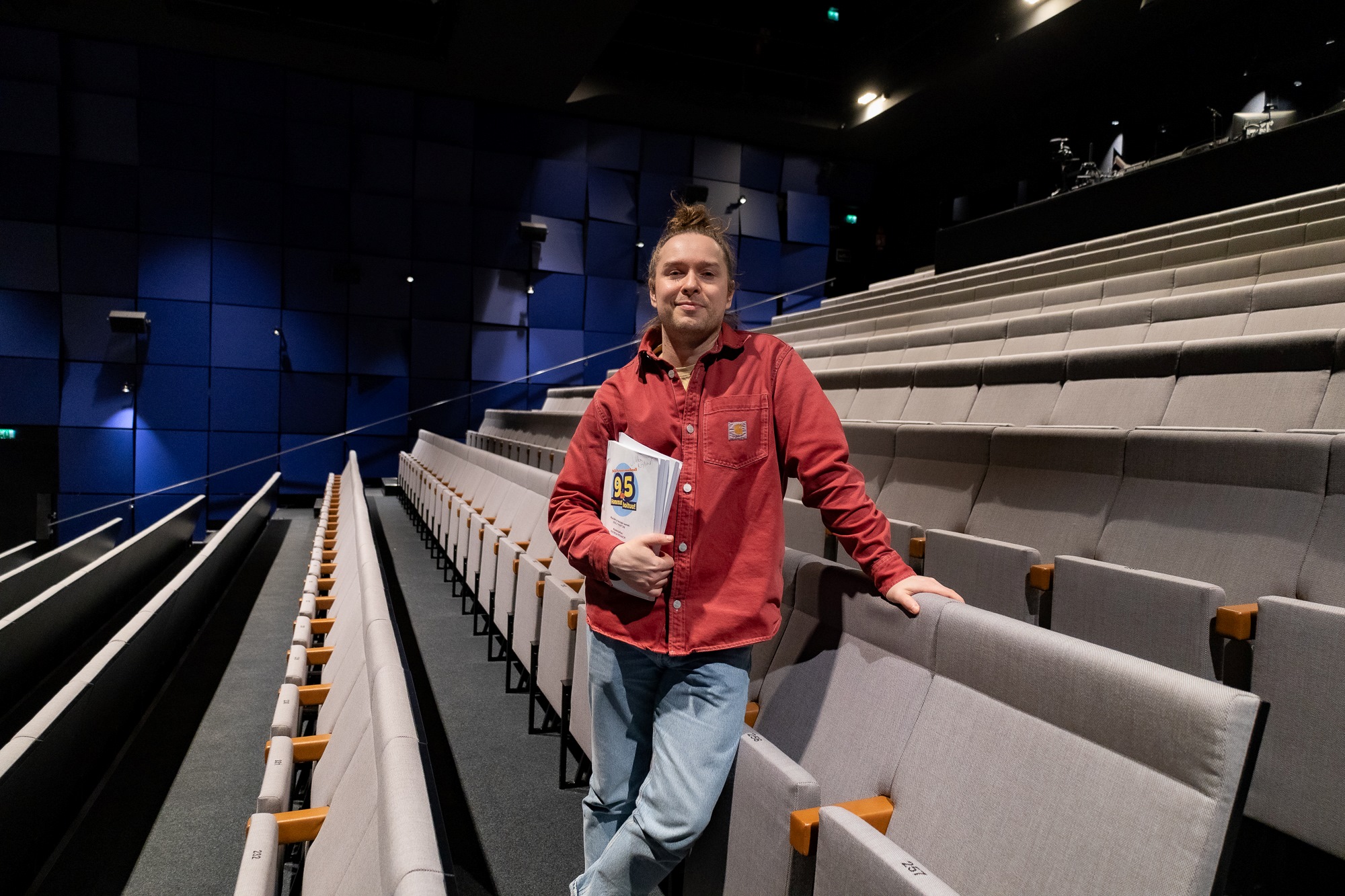 Mies seisoo rennosti teatterin katsomossa. Kädessään hänellä on musikaalin käsikirjoitus.